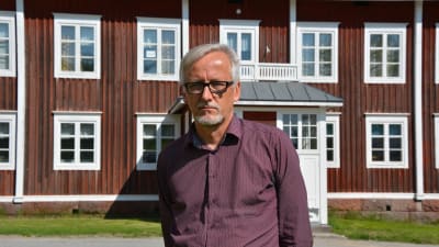 Direktör Matti Salminen på Statens skolhem står framför ett av de hundra år gamla husen på Lagmansgården i Pedersöre.