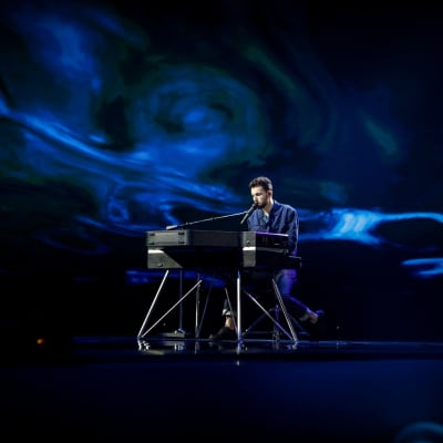 duncan laurence sjunger sittandes vid ett elpiano och har ett blått skimmer runtom sig