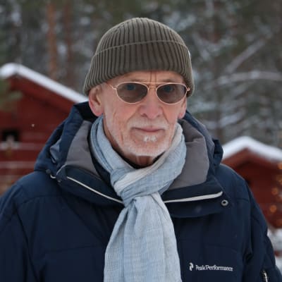 En äldre man med glasögon. Han är klädd i vinterkläder.