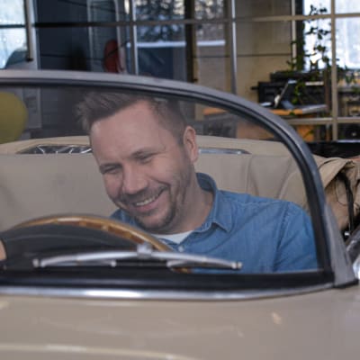 Roni Collin sitter i en gammala beige öppen Porsche. Han ler. Bilen är inomhus vid hans kontor.