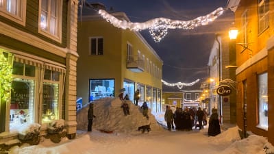 Vy i snöiga Gamla stan i Borgå. Barn leker i en stor snöhög invid Simolinshuset.
