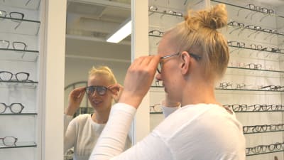 Kvinna provar glasögon framför spegel.
