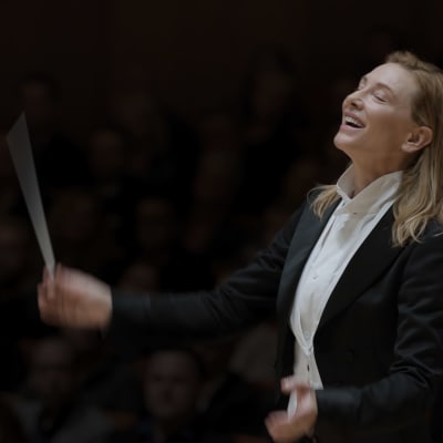 En kvinnlig dirigent höjer taktpinnen medan hon lutar sig bakåt.