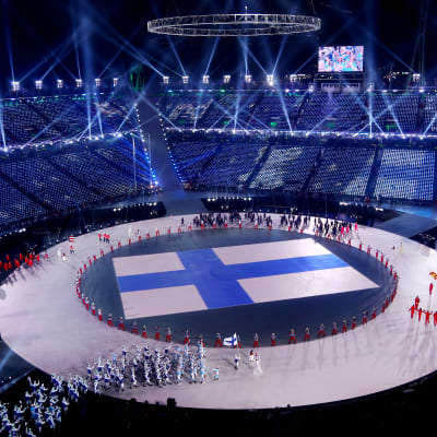 Suomen lippu isona heijasteena keskellä olympiastadionia, kun joukkueet saapuvat avajaisiin.