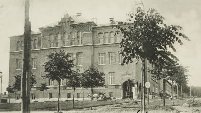 Mustavalkoisessa kuva suurikokoinen koulurakennus.