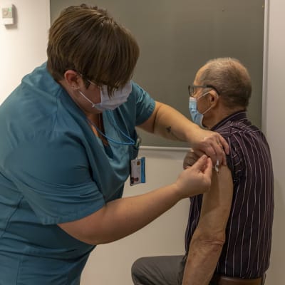 Sairaanhoitaja pistää influenssarokotteen ikääntyneen miehen olkavarteen.