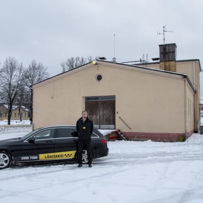 Taxichaufför Toni Ahlfors intill sin taxibil som han parkerat utanför Lovisa busstation.