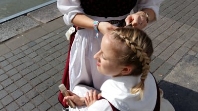 En flicka i folkdräkt får sitt hår flätat av en kompis.