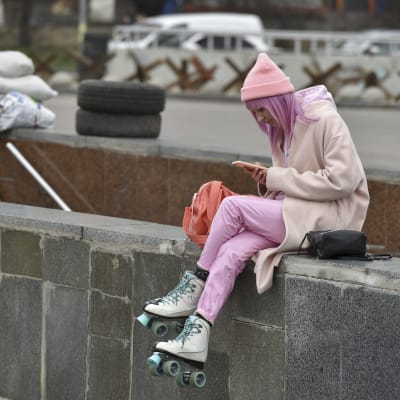 Nuori henkilö selailee puhelintaan Kiovan keskustassa rullaluistimet jalassa, taustalla tiesulku.