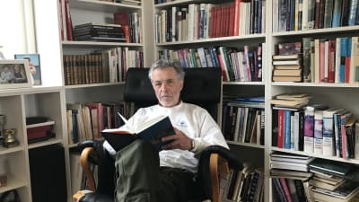 Jan-Erik Enestam sitter framför en bokhylla med en bok i handen.