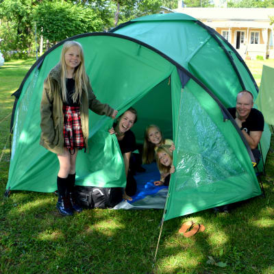 En kvinna, en man och tre barn som sitter inne och utanför ett grön tält.