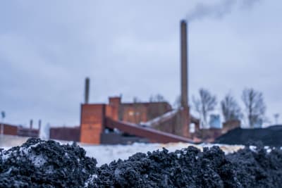 Kolkraftverket på Hanaholmen i Helsingfors fotograferat på mrknivå med svart lera eller kol i förgrunden. 