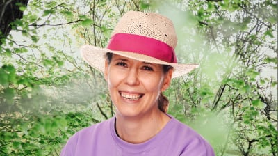 Kvinna i hatt mot somrig bakgrund.