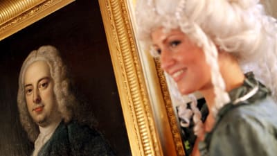 Dam i peruk visar upp en tavla som föreställer Georg Friedrich Händel