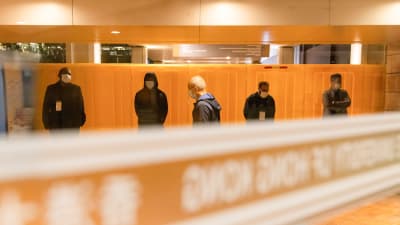 Personer i mörka kläder står vid orange vägg.