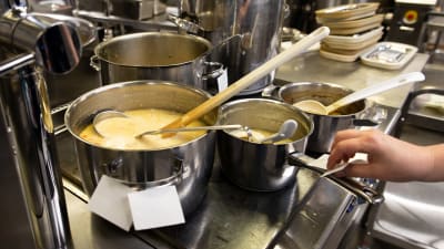Skolmat tillreds samtidigt i flera stora kastruller på en spis.