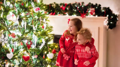 Två barn står glada vid julgranen.