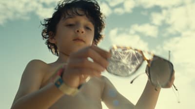 Unga pojken Trent håller upp ett par trasiga solglasögon på stranden.