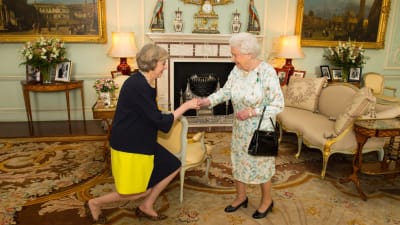 Theresa May knäböjer framför drottning Elizabeth II på Buckingham Palace.