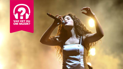 Lorde sjunger i en mikrofon som hon håller i höger hand.