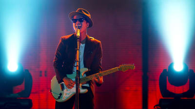 Bruno Mars på scenen med gitarr och solglasögon.