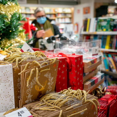 Nainen katselee joululahjoja kirjakaupassa hengityssuojain kasvoillaan.