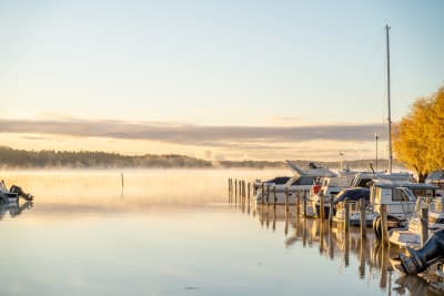 Båtar vid en båthamn en höstmorgon, på havet syns lite dimma som stiger upp.