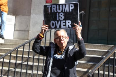 En person som håller i en skylt med texten "Trump is over" (Trump är förbi). Personen står utanför åklagarmyndighetens byggnad i News York den 20.3.2023.
