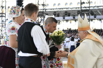 Påve Franciskus med mitra på huvudet tar emot blommor av en grupp ungrare i folkdräkt.