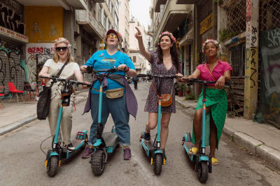 Fyra kvinnor står bredvid varandra på en mindre gata. De håller alla i varsin elsparkcykel.