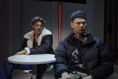 Två unga män med utmattad uppsyn sitter vid ett runt vitt bord.  