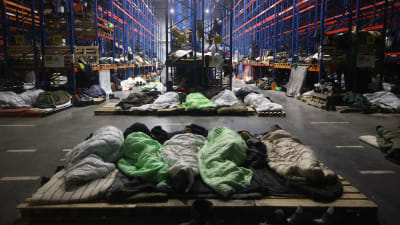 Migranter sover på rad i en lagerlokal.