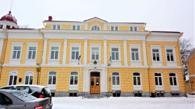 Ett gult gammalt stenhus, vinter, snö. Det står stadshus på byggnaden som har två våningar plus en mindre del högst upp i tredje våningen.