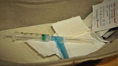 En vaccinspruta med förpackning på ett vitt papper.