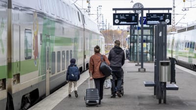 Två vuxna och ett barn går mot ett tåg på en tågstation.