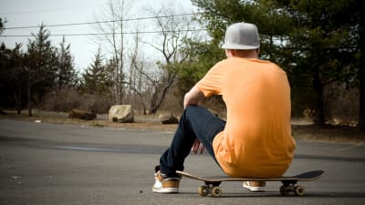En pojke sitter på en skateboard med ryggen mot kameran.