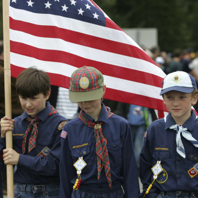 Fyra pojkar i scoutkläder står på rad. En av dem håller i den amerikanska flaggan. Resten tittar åt sidan eller neråt.