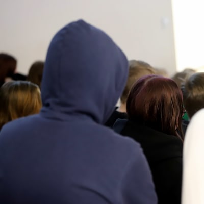 Sysmän yhteiskoulun oppilaita kuuntelemassa luentoa, kuvattu takaapäin, oppilaat eivät ole tunnistettavissa, edessä olevalla huppu päässään.