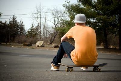En pojke sitter på en skateboard med ryggen mot kameran.