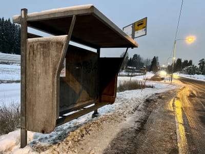 En busskur i trä vid en snöig landsväg.
