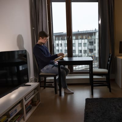opiskelija Mikko Vanhala lukee oppikirjaa ikkunan edessä vuokrayksiössään.