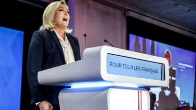 Marine Le Pen står och talar framför ett podium.