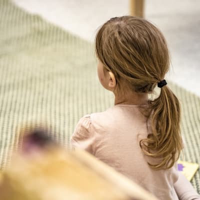 Anonym bild från ett daghem. En flicka sitter på knä med ryggen vänd mot kameran. 
