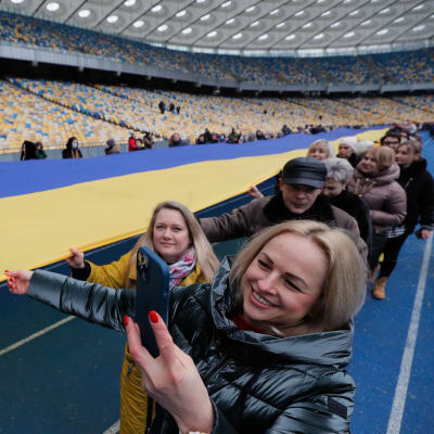 Män och kvinnor håller i en väldig ukrainsk flagga