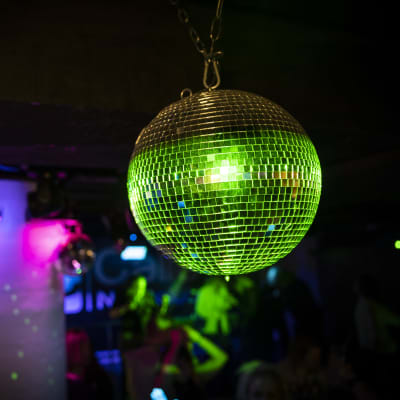En discoboll lyser grön ovanför ett dansgolv.