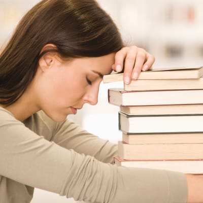 Kvinna lutar sig trött mot en trave böcker.