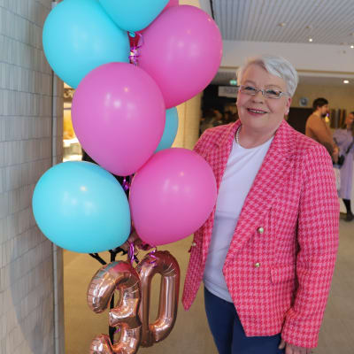En person i rosa kavaj håller i ett knippe ballonger. 