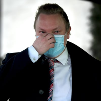 Kulturminister Antti Kurvinen med munskydd på sig. Han står framför Ständerhusets dörr och pratar med reportrar.