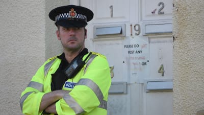 En brittisk polis står med korsade armar och vaktar ett bostadsområde i Manchester.