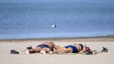 Två personer solbadar på en sandstrand.